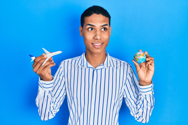 Young african american guy holding paper plane and world ball smiling looking to the side and staring away thinking royalty free stock photos