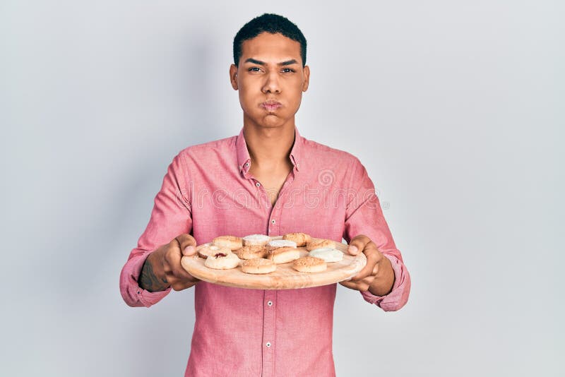 Young african american guy holding tray with cake sweets puffing cheeks with funny face stock photos