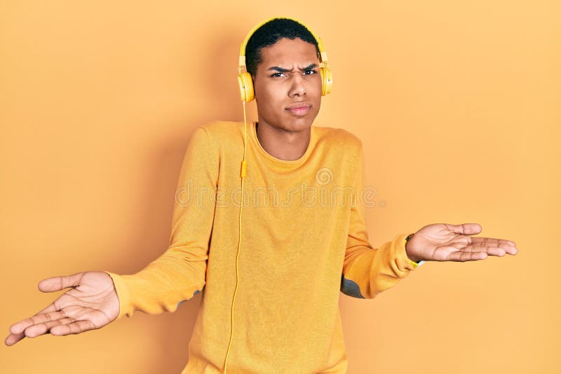 Young african american guy listening to music using headphones clueless and confused with open arms, no idea concept royalty free stock photo