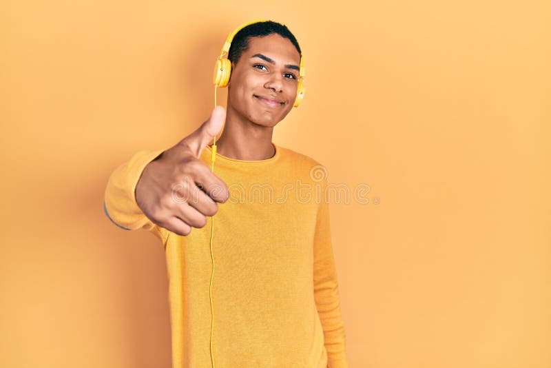 Young african american guy listening to music using headphones doing happy thumbs up gesture with hand stock photo