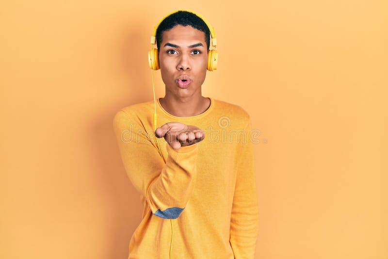 Young african american guy listening to music using headphones looking at the camera blowing a kiss with hand on air being lovely stock photography