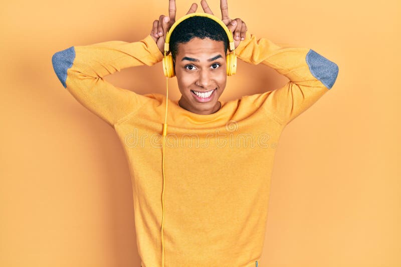 Young african american guy listening to music using headphones posing funny and crazy with fingers on head as bunny ears, smiling stock photos