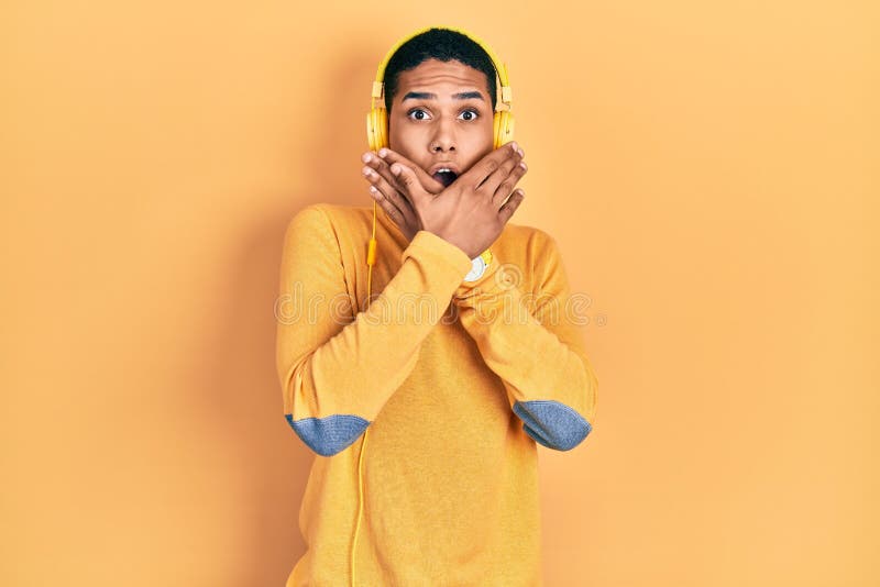 Young african american guy listening to music using headphones shocked covering mouth with hands for mistake stock images