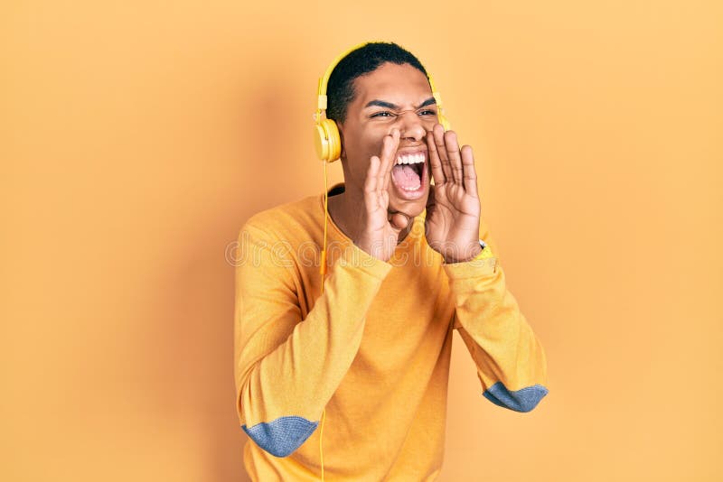 Young african american guy listening to music using headphones shouting angry out loud with hands over mouth stock photo