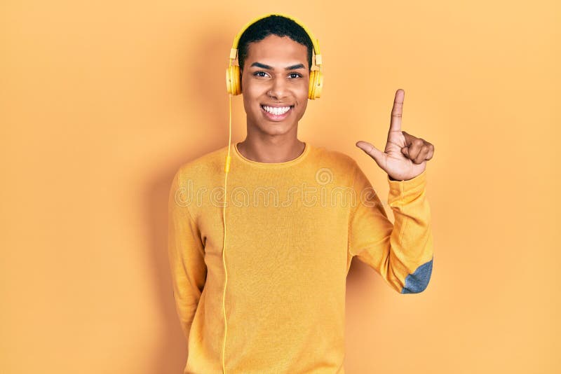 Young african american guy listening to music using headphones showing and pointing up with fingers number two while smiling stock photos
