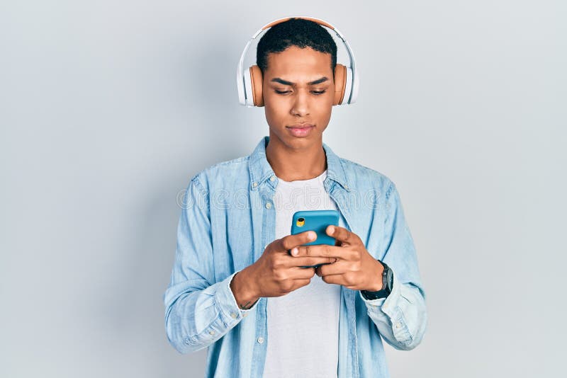 Young african american guy using smartphone wearing headphones thinking attitude and sober expression looking self confident stock photo