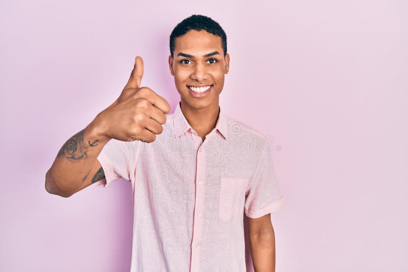 Young african american guy wearing casual clothes smiling happy and positive, thumb up doing excellent and approval sign stock photo