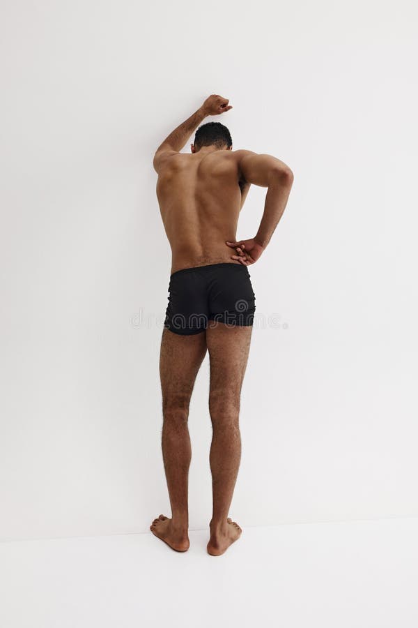 Young African-American man with relief strong back, muscular body standing shirtless in black boxers isolated on white background. Concept of male beauty, sport, body care, health, fitness. Young African-American man with relief strong back, muscular body standing shirtless in black boxers isolated on white background. Concept of male beauty, sport, body care, health, fitness