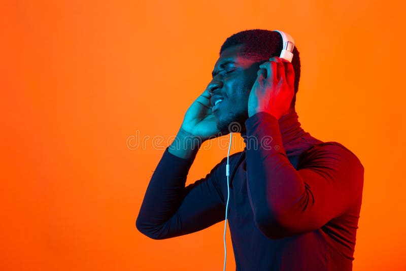 Young african-american man`s listening to music in headphones in neon light. Male portrait. Concept of human emotions