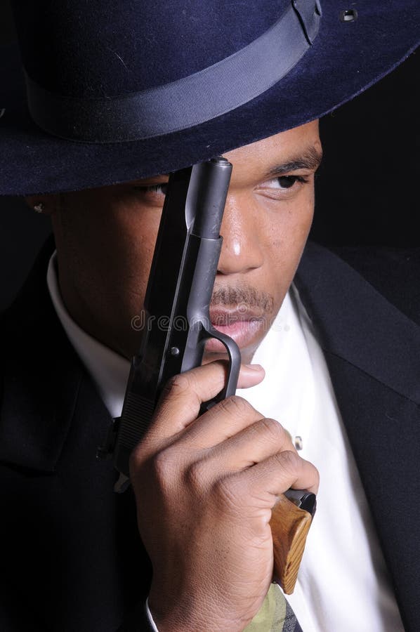 Young African American man in a hat and suit with a semi automatic pistol. Young African American man in a hat and suit with a semi automatic pistol