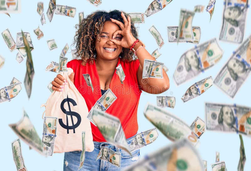 Young african american plus size woman holding money bag with dollar symbol smiling happy doing ok sign with hand on eye looking stock photo