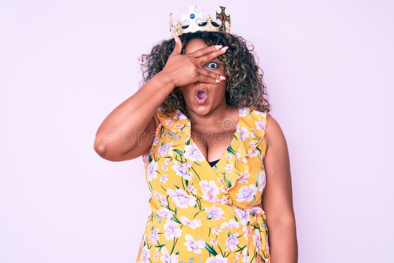 Young african american plus size woman wearing princess crown peeking in shock covering face and eyes with hand, looking through royalty free stock photos