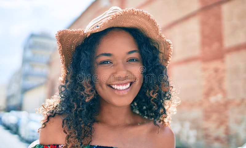 Young african american woman with curly hair smiling happy outdoors wearing summer hat royalty free stock images