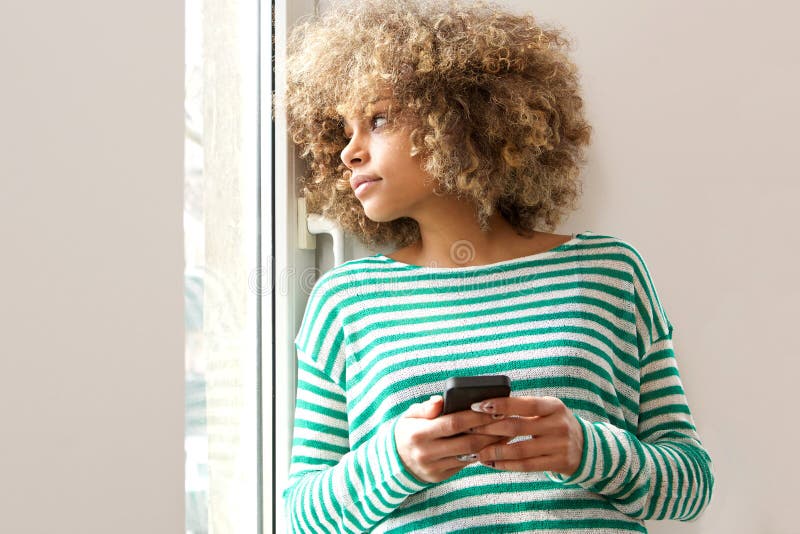 Young african american woman holding mobile phone and looking out window