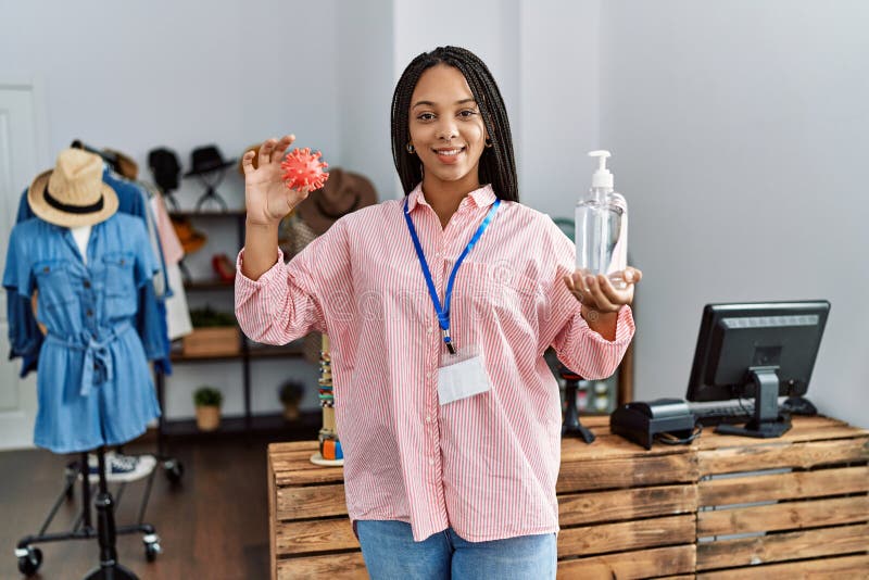 Young african american woman holding virus toy and sanitizer gel hands working at clothing store