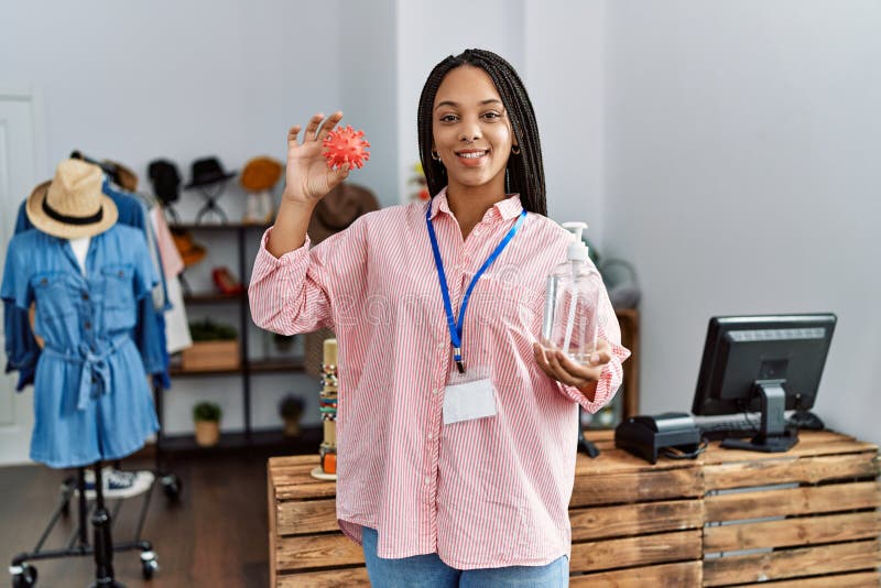 Young african american woman holding virus toy and sanitizer gel hands working at clothing store