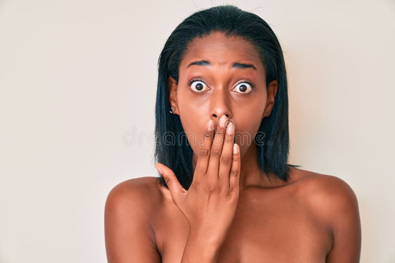 Young african american woman naked over background covering mouth with hand, shocked and afraid for mistake stock photo