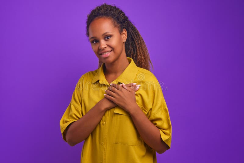 Young African American woman volunteer puts palms on heart stands in studio