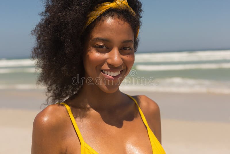 Portrait of happy young African American woman in yellow bikini looking at camera standing on the beach. She is smiling. Portrait of happy young African American woman in yellow bikini looking at camera standing on the beach. She is smiling