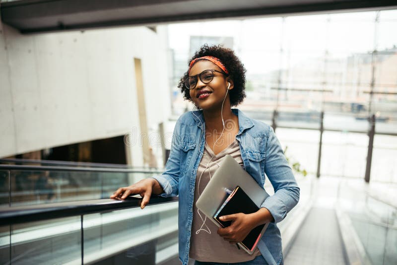 Young African female entrepreneur riding an escalator in an offi