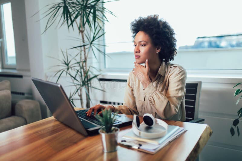 Young African female entrepreneur sitting at a desk in her home office working online with a laptop