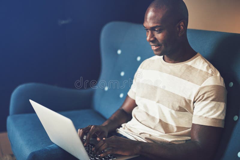 Smiling African entrepreneur sitting on a couch working online royalty free stock photo Smiling African entrepreneur sitting on a couch working online royalty free stock photo