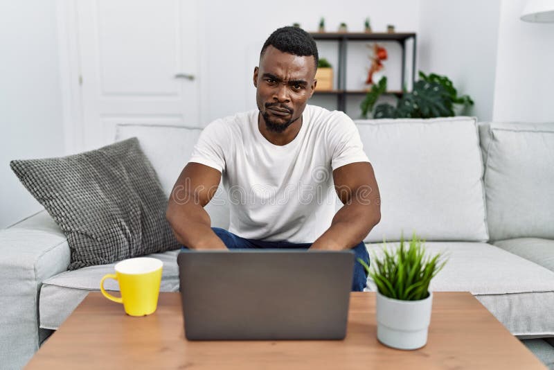 Young african man using laptop at home skeptic and nervous, frowning upset because of problem