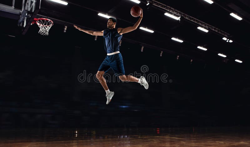 Young African sportsman, basketball player training in gym, idoors isolated on dark background. Concept of sport, game