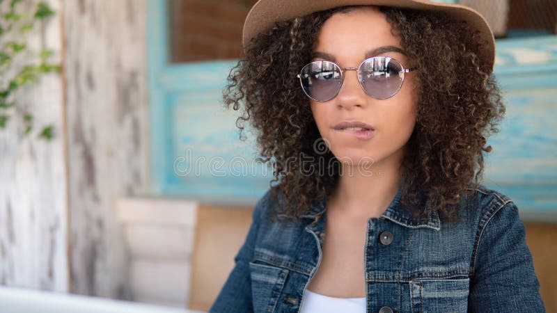 Young Afro-American woman in glasses and hat biting a lip, wearing jeans jacket royalty free stock photo Young Afro-American woman in glasses and hat biting a lip, wearing jeans jacket royalty free stock photo