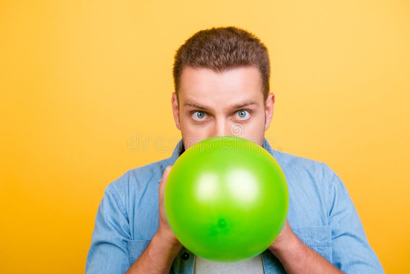 Young, amazed, stylish blond man is blowing green balloon for bi