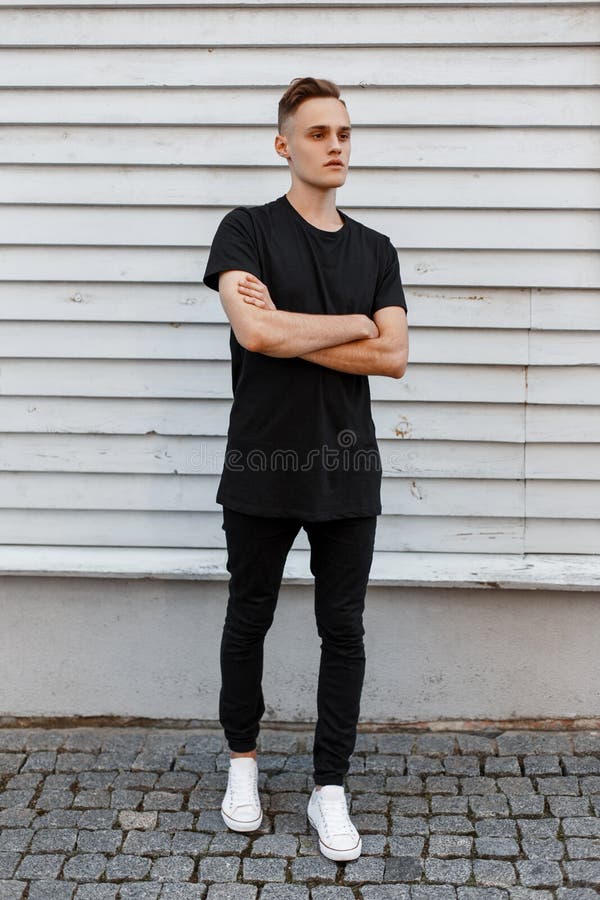 Young Amazing Stylish Man in a Black Stylish T-shirt in Trendy Jeans in  White Sneakers Poses Near a White Wooden Vintage House. Stock Photo - Image  of adult, backpack: 139128040