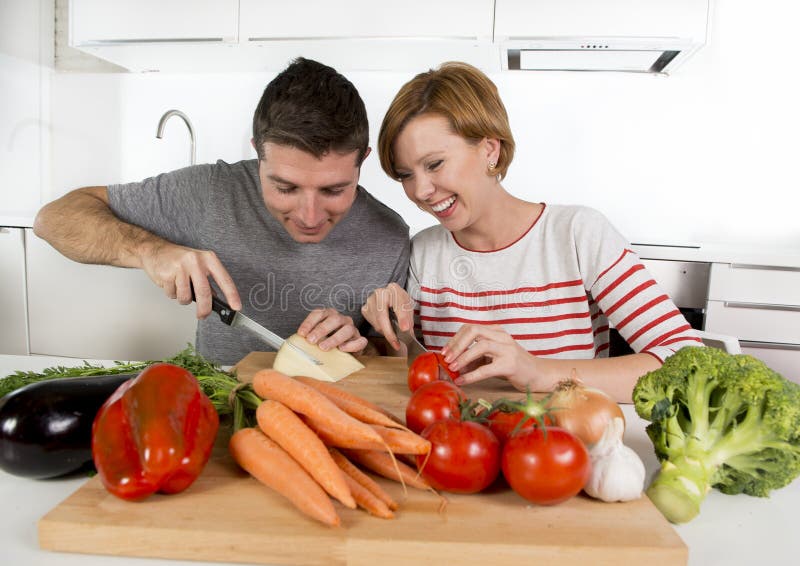 Young American couple working at home kitchen preparing vegetable salad together smiling happy