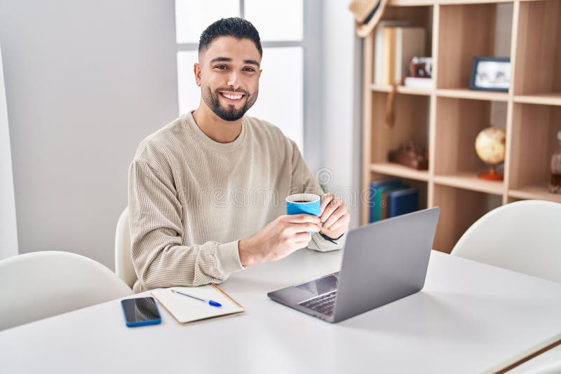 Young Arab Man Drinking Coffee Sitting on Table Studying at Home Stock