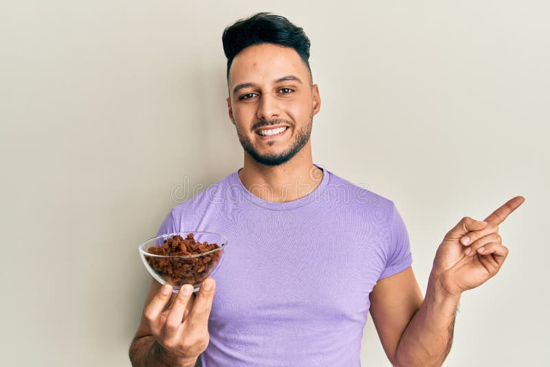 Young arab man holding raisins bowl smiling happy pointing with hand and finger to the side stock images
