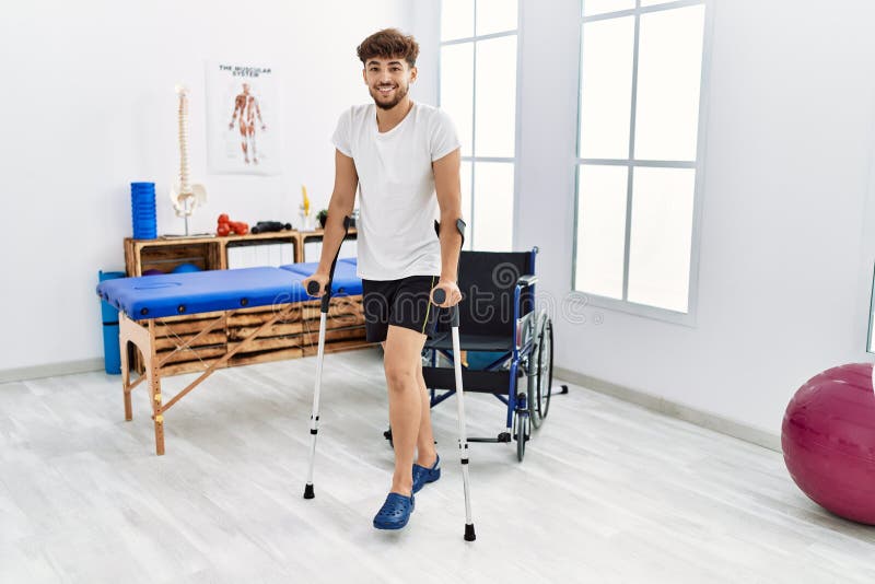 Young Arab Man Patient Walking Using Crutches at Clinic Stock Image