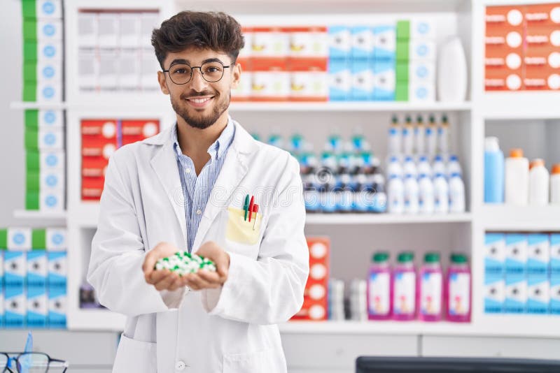 Young Arab Man Pharmacist Smiling Confident Holding Capsules at