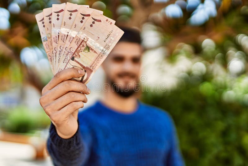 Young arab man smiling confident holding riyal banknotes at park royalty free stock photos