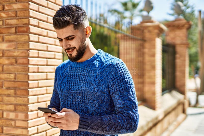 Young arab man smiling happy using smartphone at street stock photography