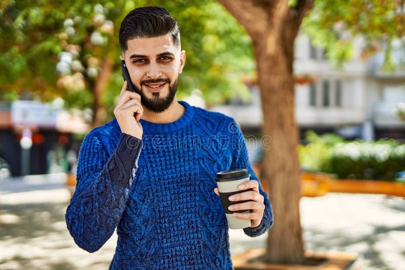 Young arab man talking on the smartphone drinking coffee at park stock photo