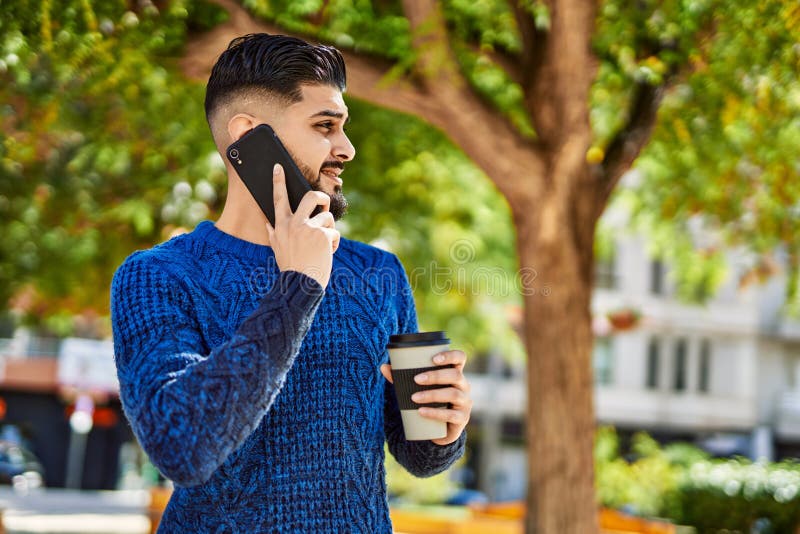 Young arab man talking on the smartphone drinking coffee at park stock photo