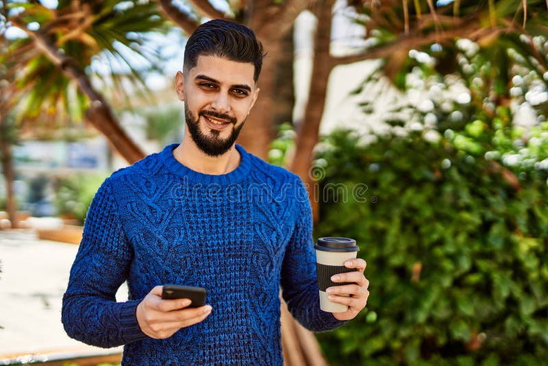 Young arab man using smartphone drinking coffee at park royalty free stock photo