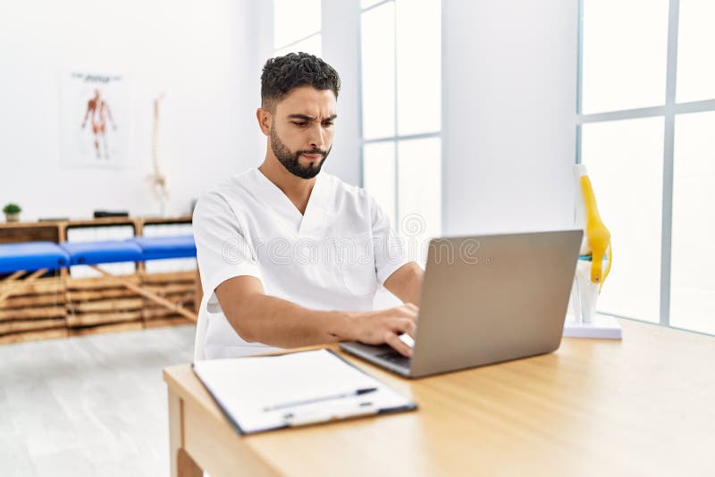 Young Arab Man Wearing Physiotherapist Uniform Using Laptop at Clinic Stock Photo Image of