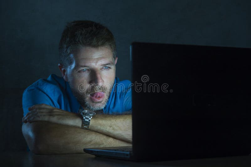 Young Aroused and Excited Sex Addict Man Watching Mobile Online in Laptop Computer Light Night at Home in Stock Photo