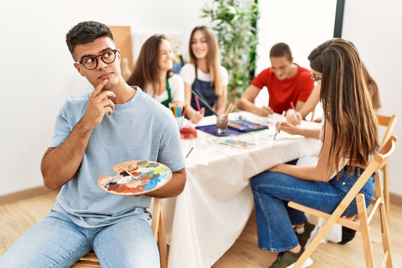 Young artist man drawing at art studio serious face thinking about question with hand on chin, thoughtful about confusing idea royalty free stock photo