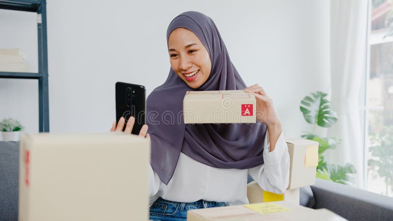 Young Asia muslim businesswoman blogger using mobile phone camera to recording vlog video live streaming review product at home office. Small business owner, start up online market delivery concept. Young Asia muslim businesswoman blogger using mobile phone camera to recording vlog video live streaming review product at home office. Small business owner, start up online market delivery concept
