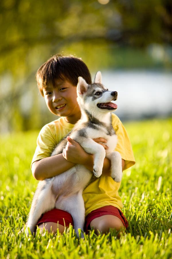 Young Asian boy hugging puppy sitting on grass