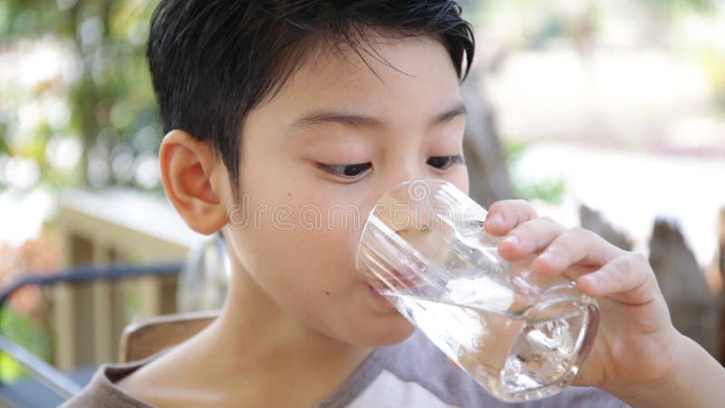 Young Asian child drinking a glass of water .