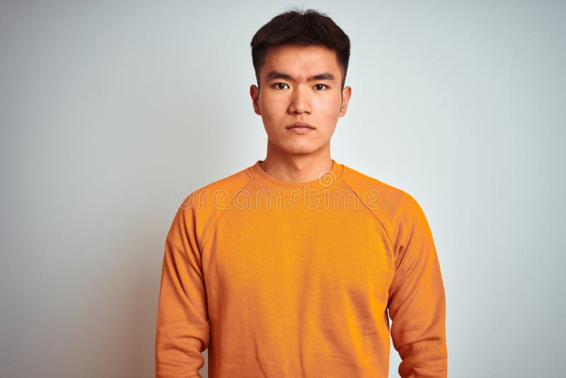 Young asian chinese man wearing orange sweater standing over isolated white background with serious expression on face stock photos