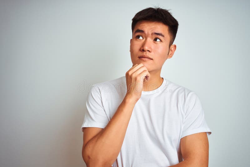 Young asian chinese man wearing t-shirt standing over isolated white background with hand on chin thinking about question, pensive stock photography