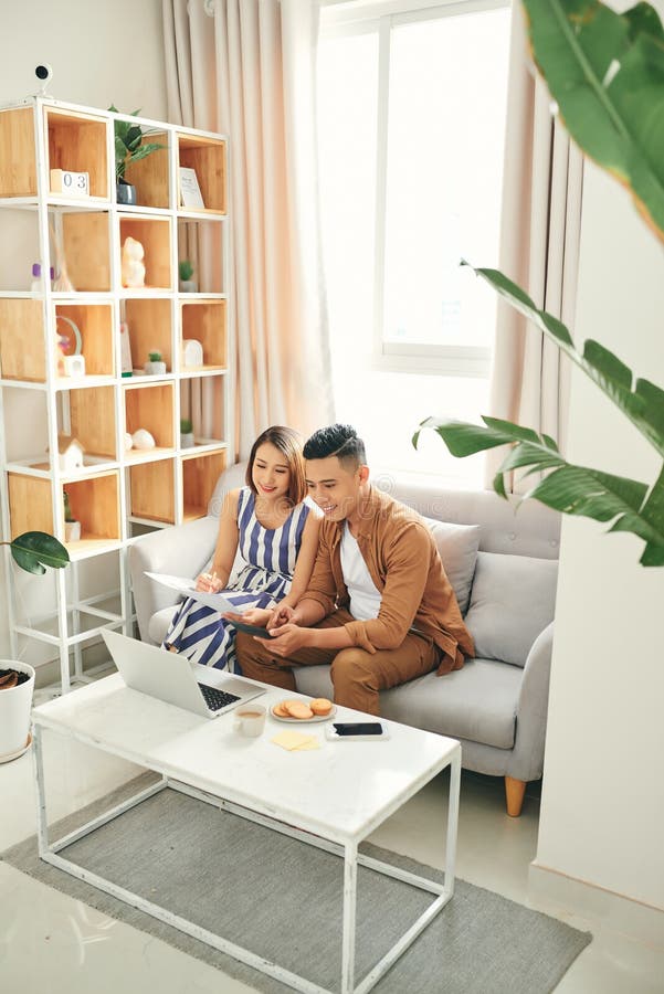 Young Asian couple organizing their bills when sitting on sofa